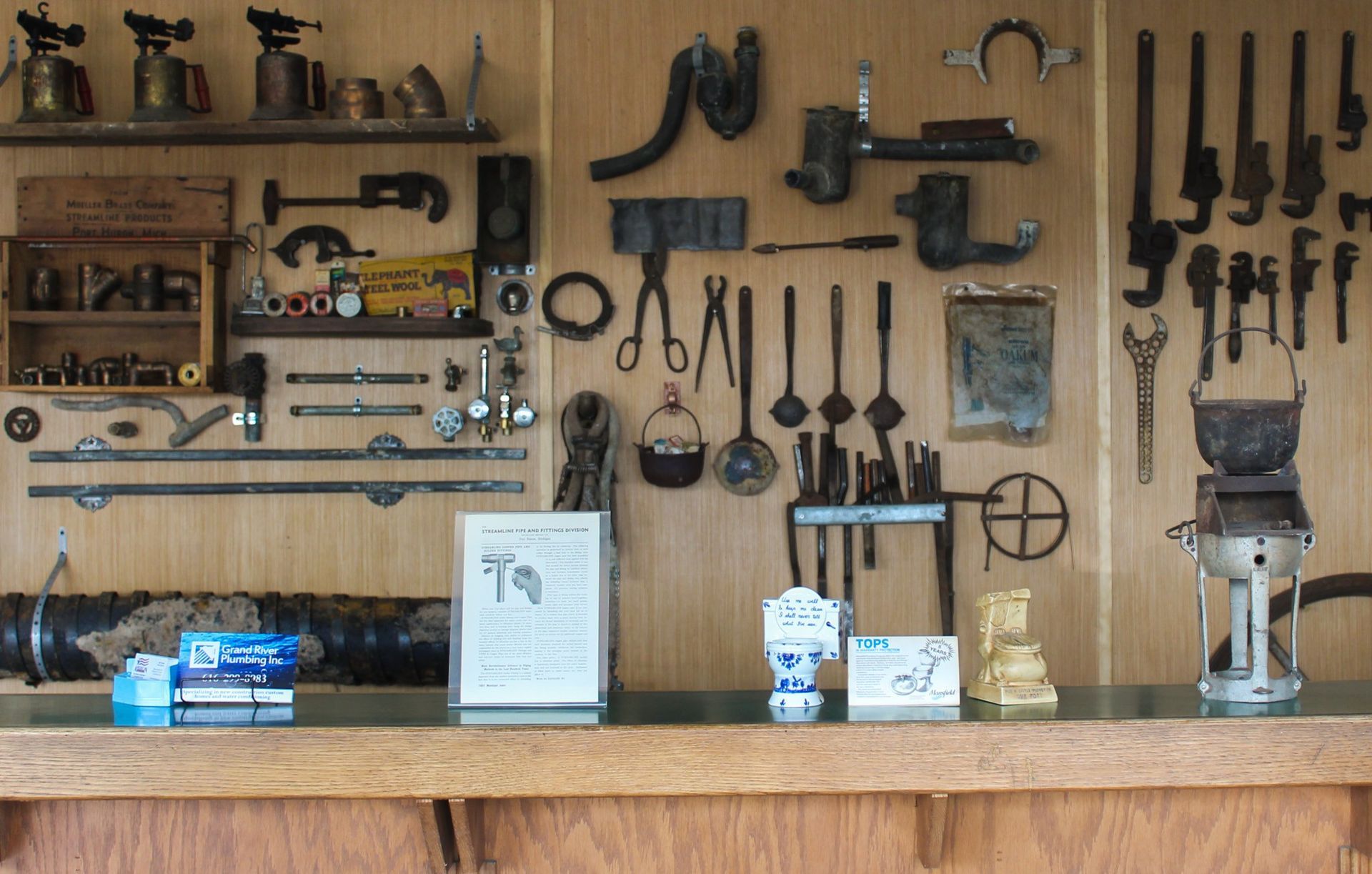 Wall-mounted display of vintage tools and hardware above a wooden workbench in a workshop.