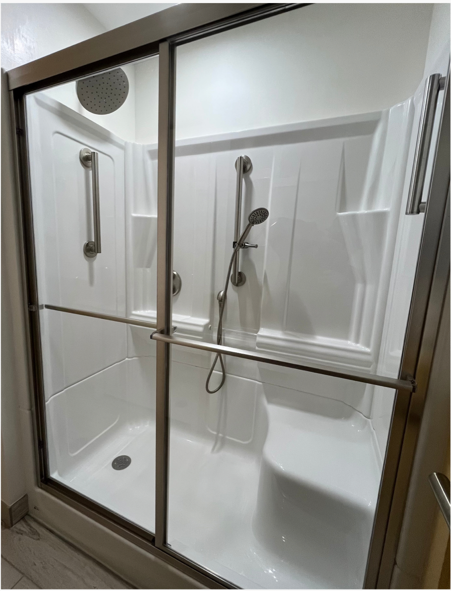 Accessible walk-in shower with glass doors, white walls, grab bars, and a handheld showerhead.