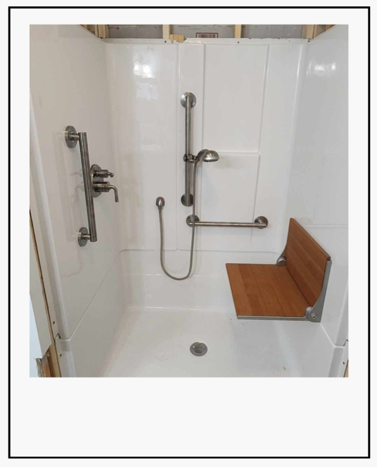 Accessible shower stall with grab bars, handheld shower, built-in seat, and white tile walls