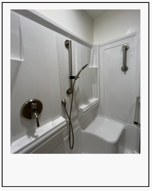 White accessible shower with grab bars and handheld showerhead in a small bathroom