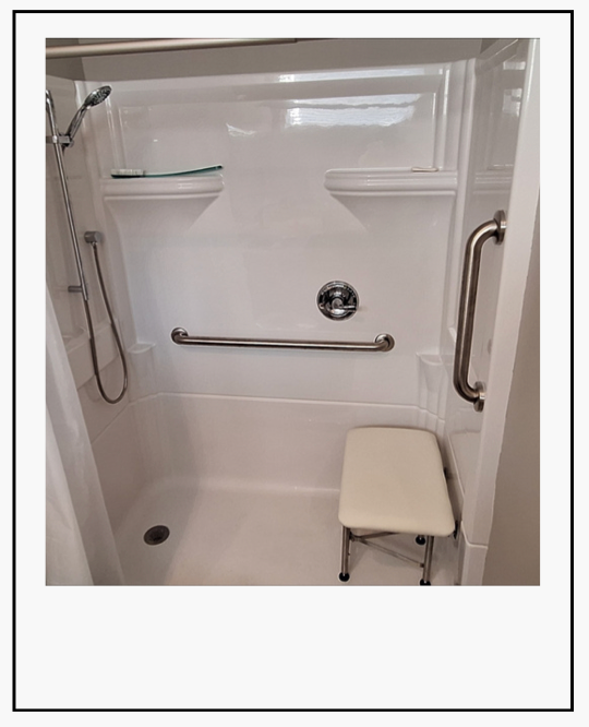 Accessible shower stall with grab bars, wall-mounted seat, and handheld showerhead.