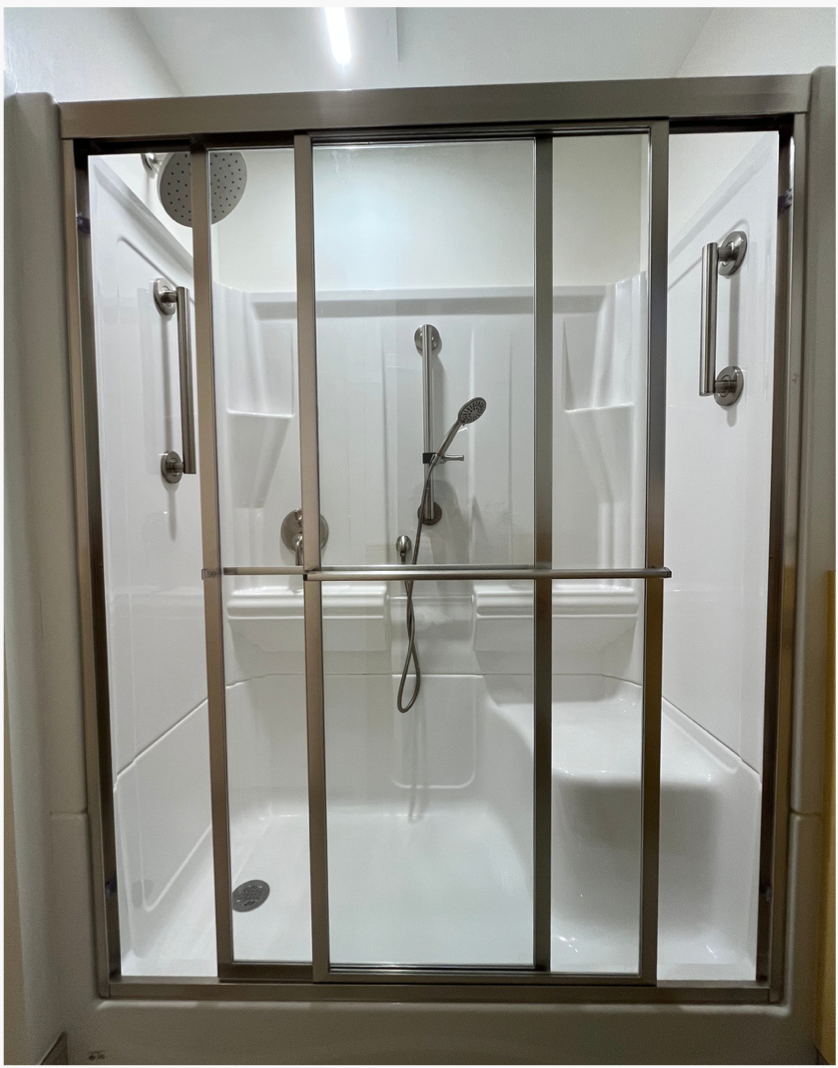 Walk-in shower with glass sliding doors, chrome grab bars, and white tiled walls