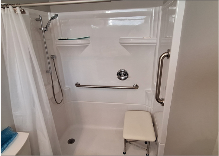 Accessible shower stall with grab bars, fold-down seat, handheld shower, and built-in shelf