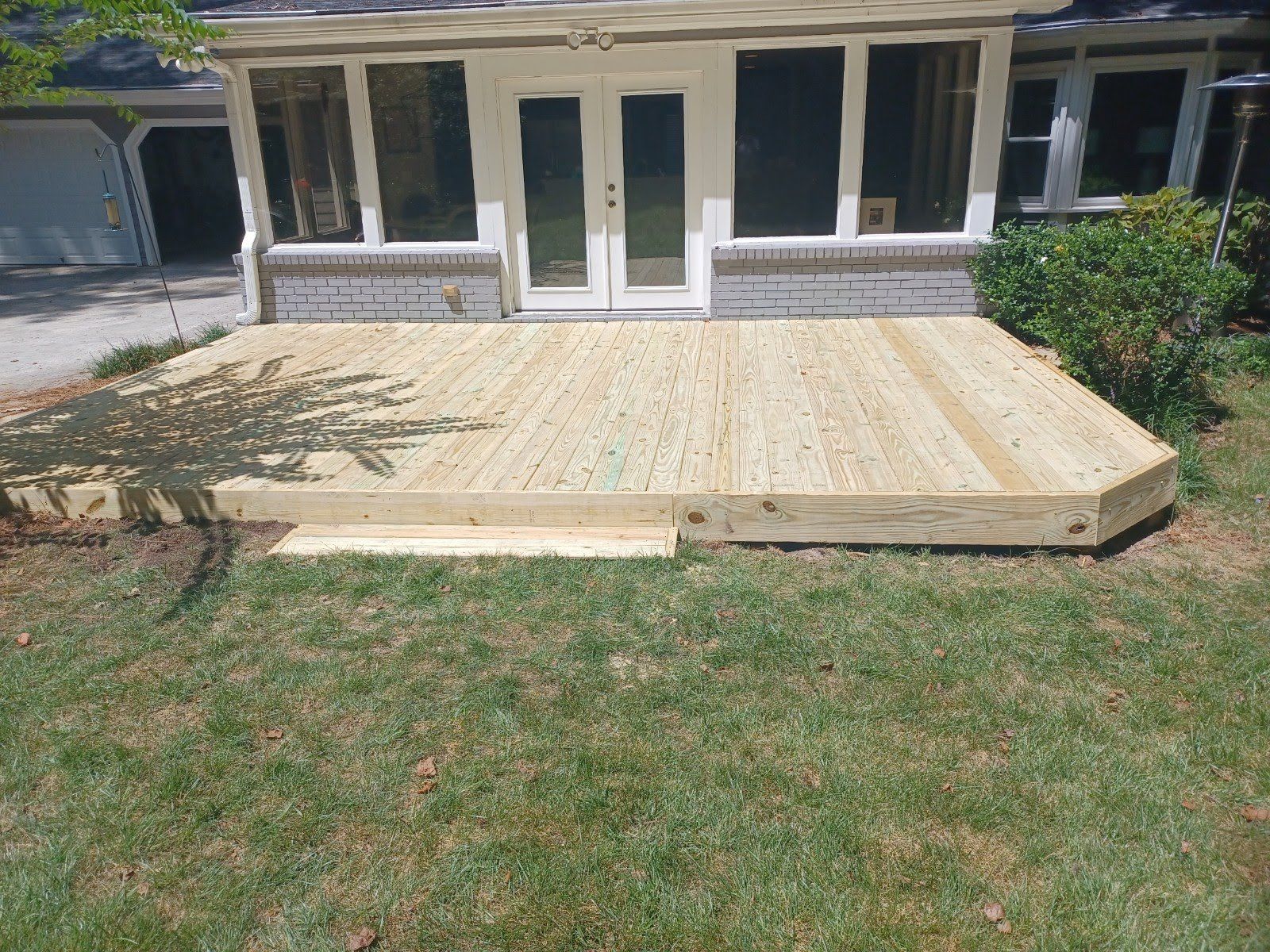 Wooden deck with steps leading to a house with white doors and windows; grass lawn in foreground.