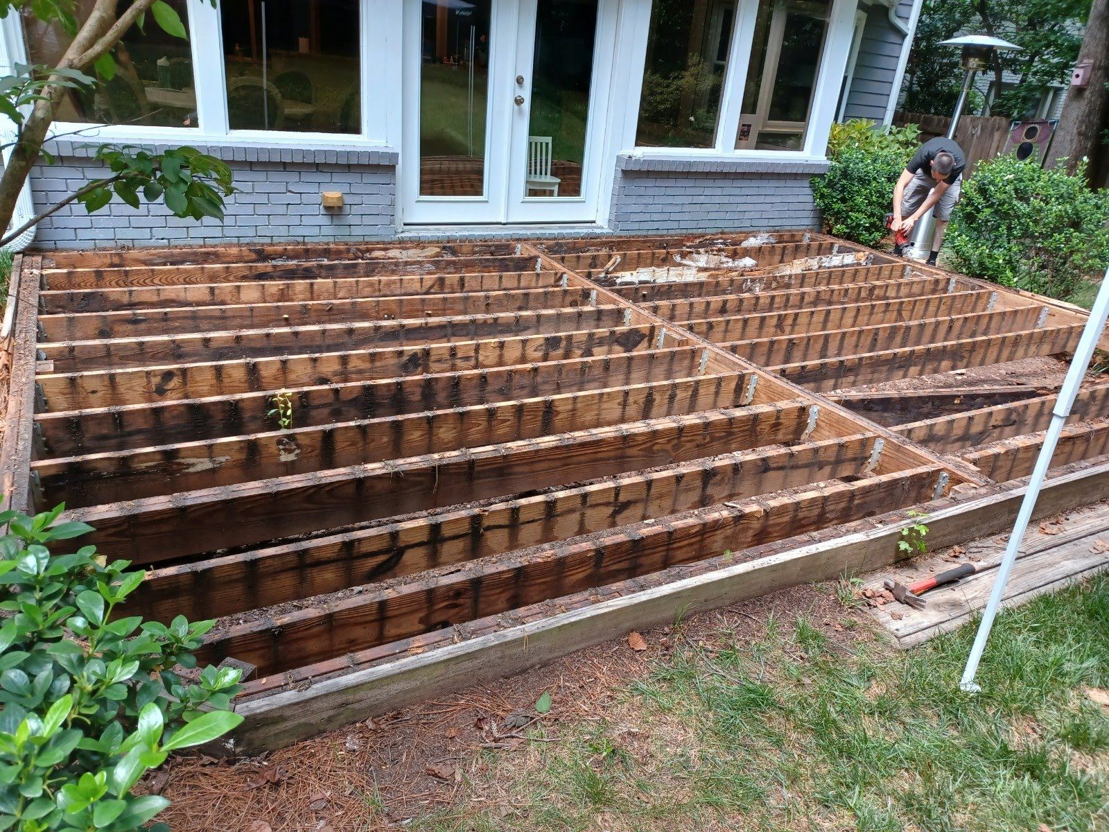 Wooden deck frame in yard, partially dismantled with a person working in the background.