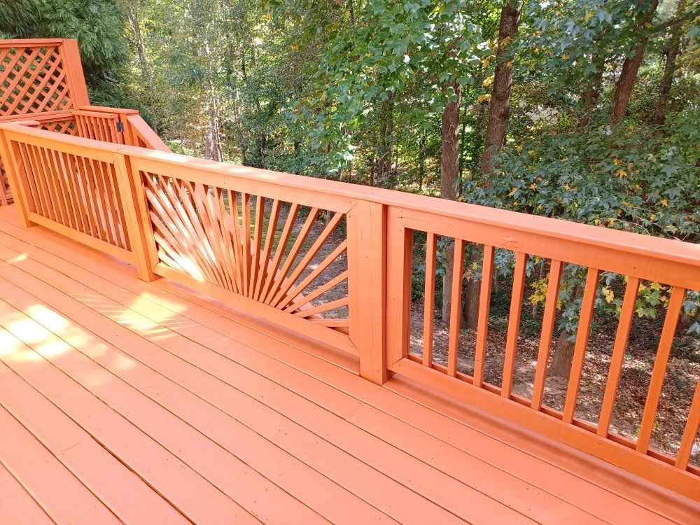 Orange painted deck with railing detail against a green tree backdrop.