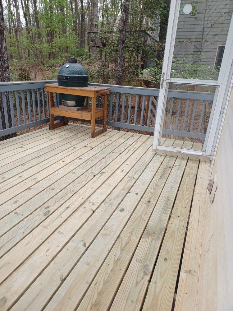 Wooden deck with a Big Green Egg grill on a wooden stand, surrounded by a gray railing.