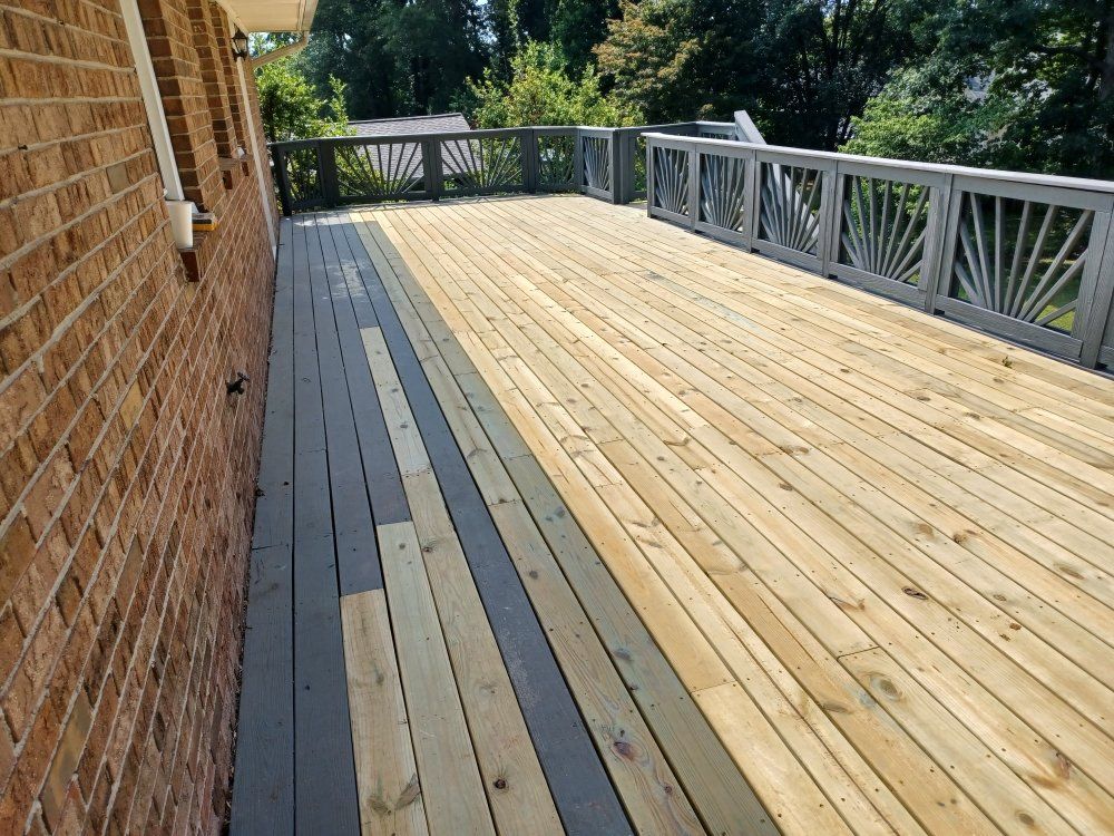 Wooden deck with gray accents next to a brick wall, surrounded by decorative railings and trees.
