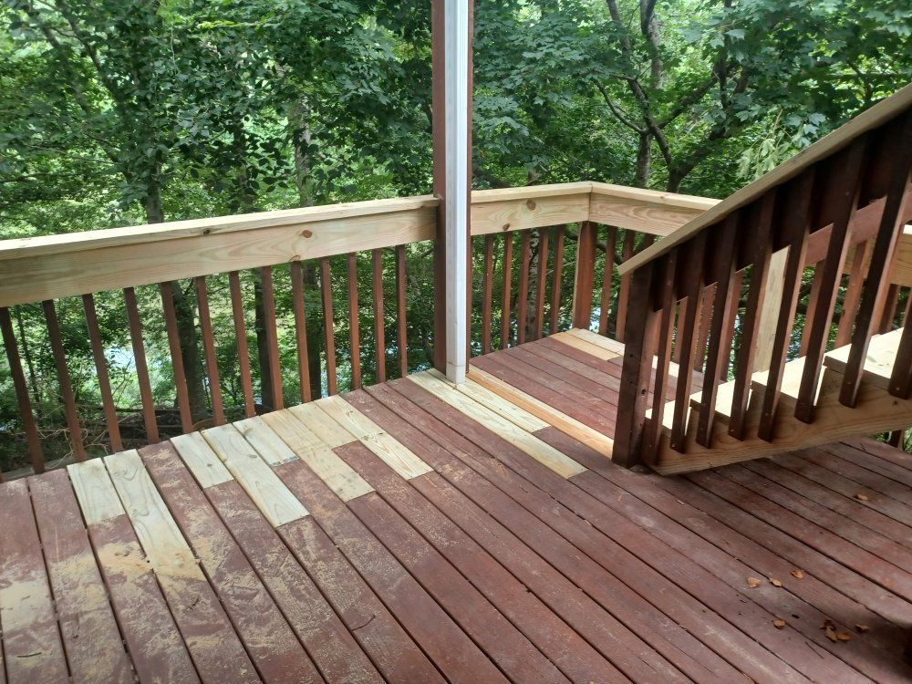 Deck with light-colored, replaced boards on dark wood, leading to a staircase, overlooking a wooded area.