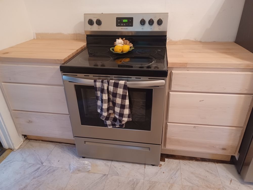 Stainless steel oven between two wooden cabinets, unfinished countertop, and a checkered towel.
