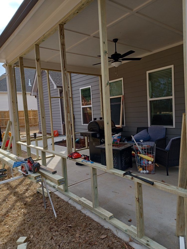 Wooden frame construction on a patio with a ceiling fan, grill, and outdoor furniture.