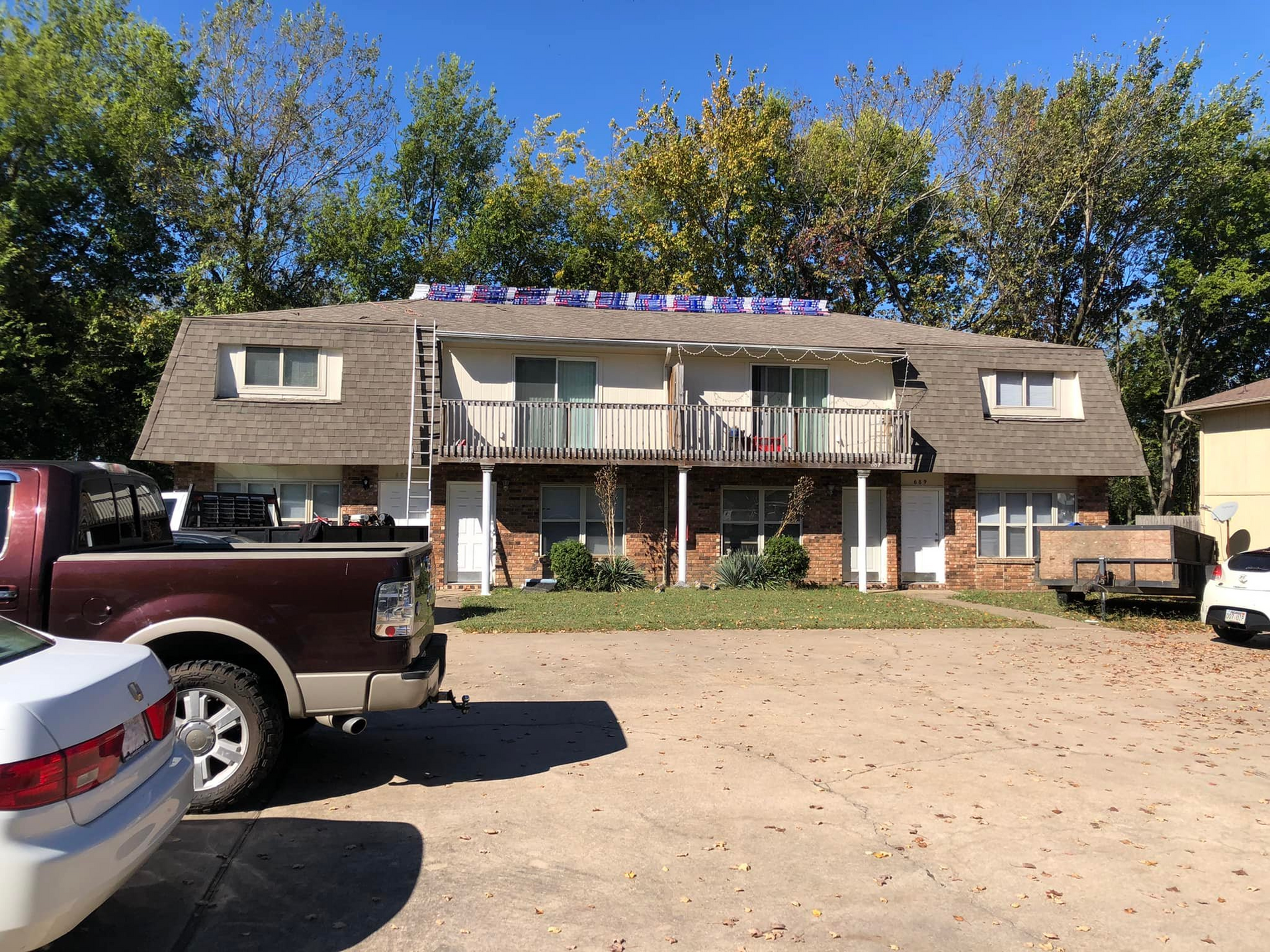 Apartment building with parked trucks and cars in a dirt lot under clear blue sky