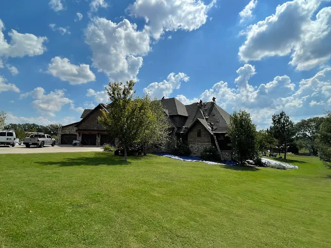 Large stone house with a steep roof on a green lawn under a blue sky with clouds