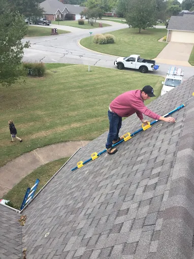 Worker on a roof using a ladder, with a suburban street and parked truck below.