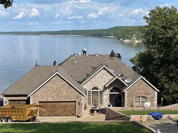 Brick lakeside house with workers on the roof and a yellow truck in front