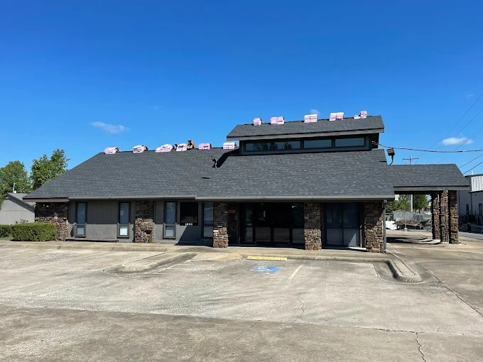 Single-story dark building with a large paved parking lot under a clear blue sky