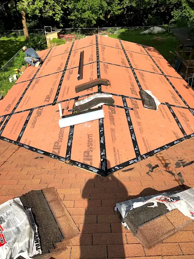Roof under repair with orange underlayment, scattered shingles, and tools on a sunny day