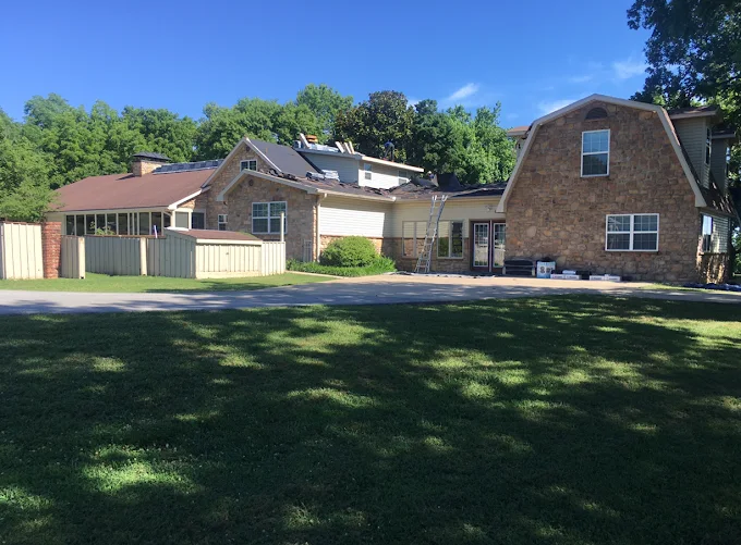 Large stone house and attached garage beside a grassy lawn under a clear blue sky