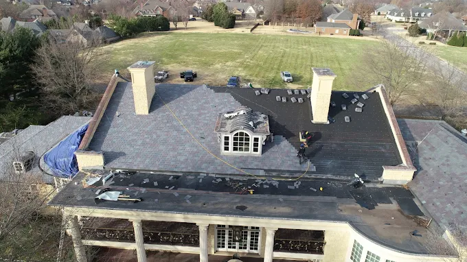 Aerial view of a house roof with chimneys, skylight, and visible roof damage or repairs.