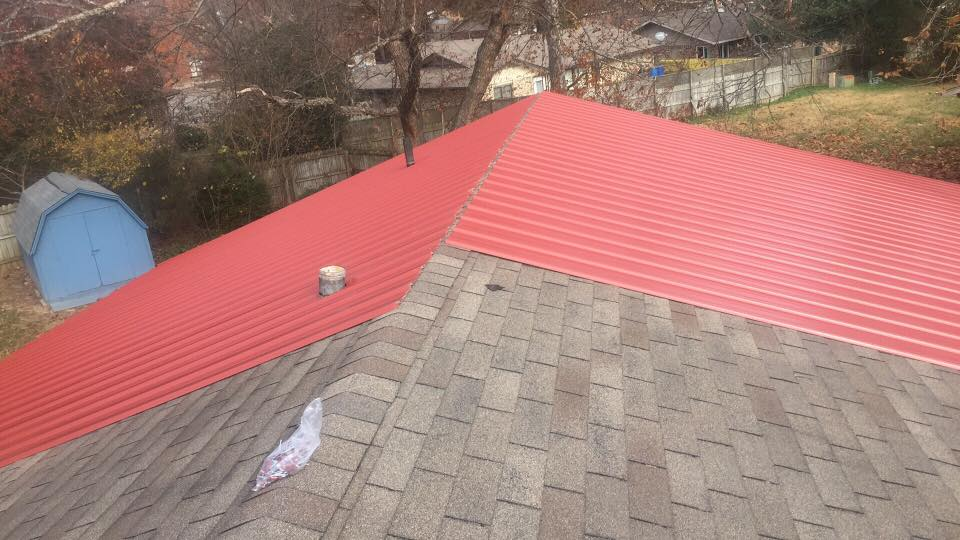 House roof with gray shingles and a red metal roof section in a wooded yard