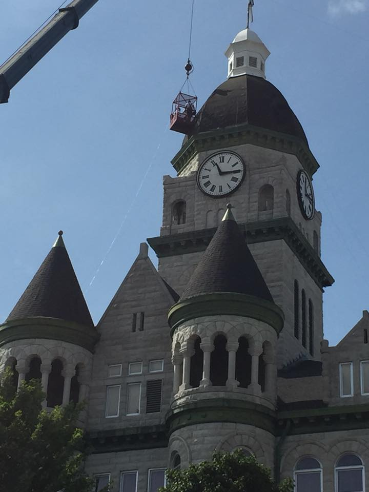 Historic stone clock tower with turrets under a blue sky, with a crane arm at left