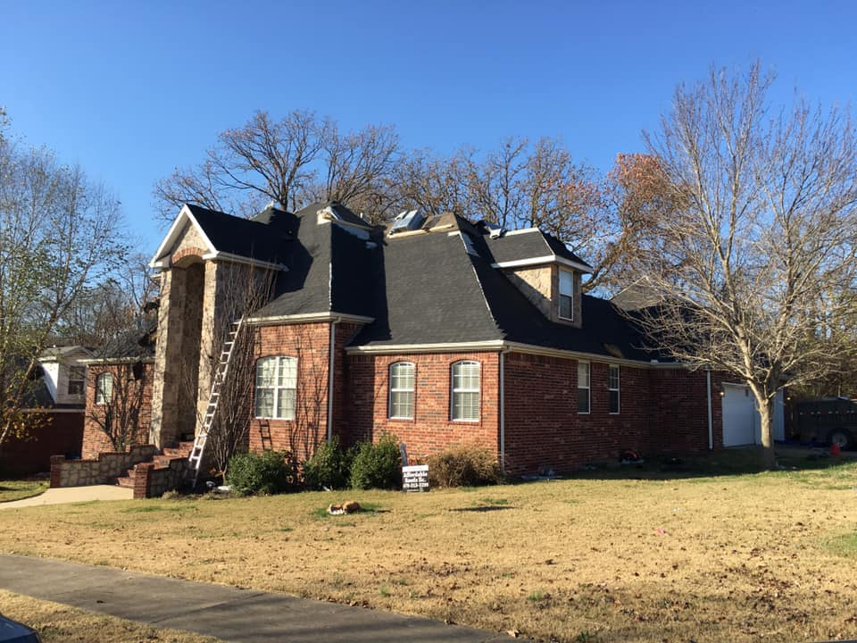 Brick house with dark roof and white trim on a sunny lawn with leafless trees.