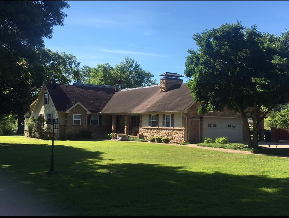 Suburban brick house with a large green lawn and trees under a bright blue sky