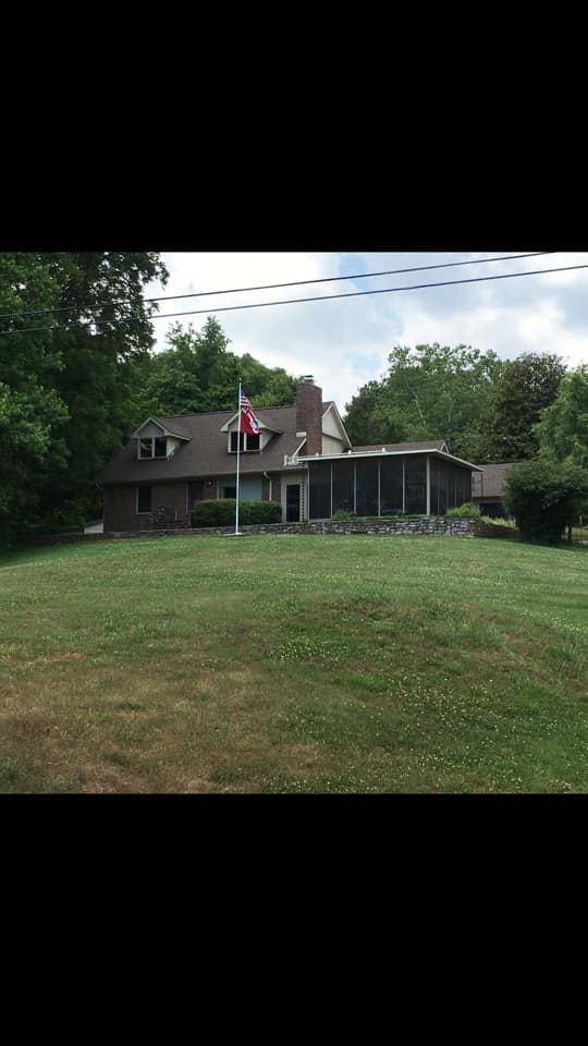 Suburban house with a screened porch, American flag, and large grassy front yard beneath trees