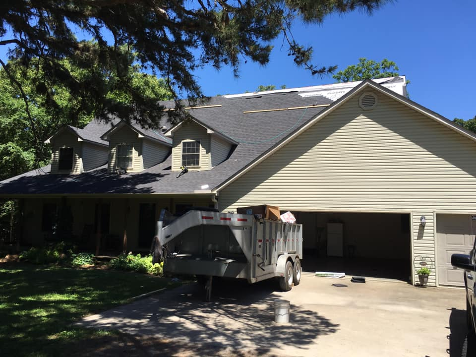 Suburban house with beige siding, open garage, and a utility trailer parked in the driveway.
