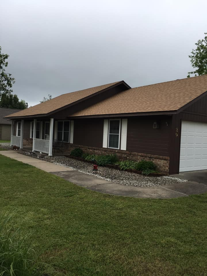 Single-story brown house with a front porch and sloped roof on a cloudy day