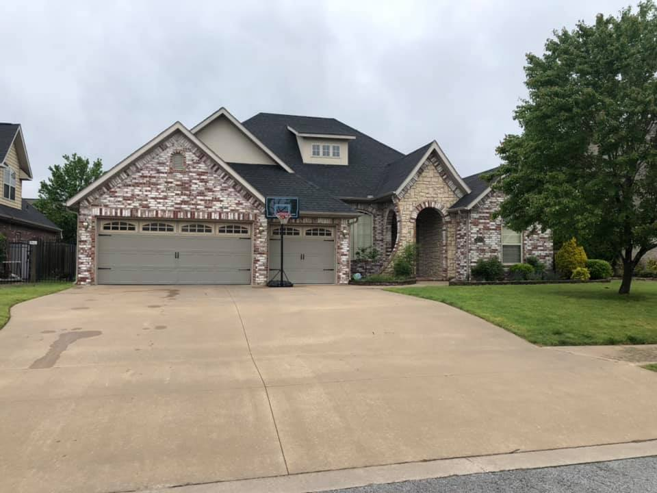 Suburban brick house with a three-car garage and wide concrete driveway under a cloudy sky