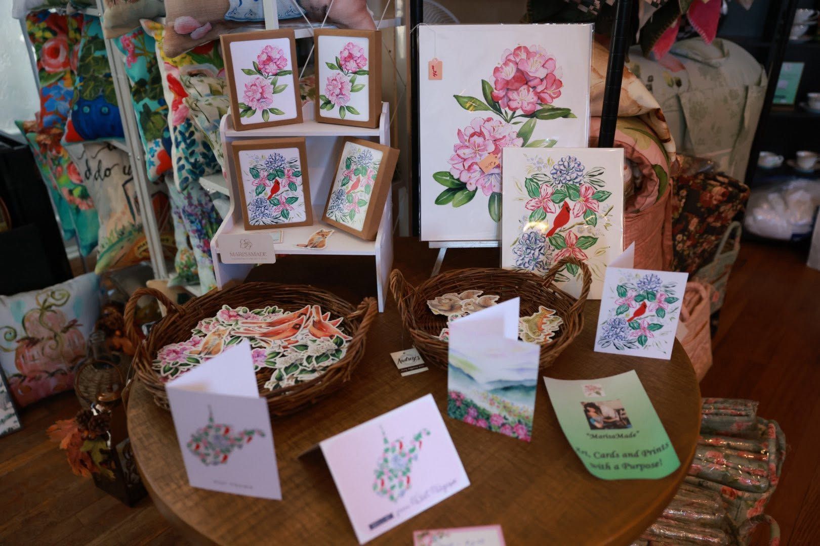 Greeting cards with colorful floral illustrations displayed on a wooden table and in a basket.