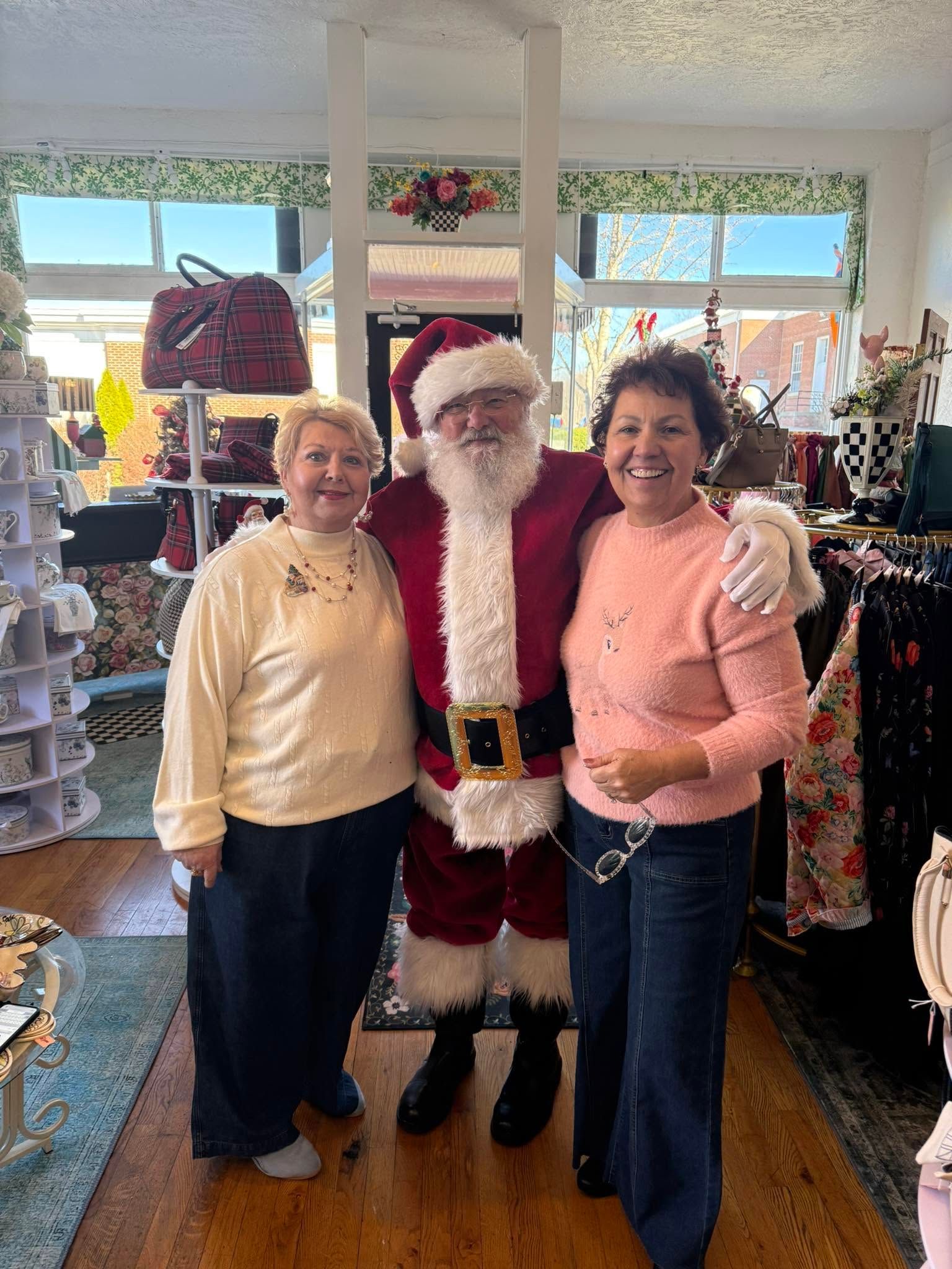 Santa standing between two women in a shop, all smiling for a holiday photo.
