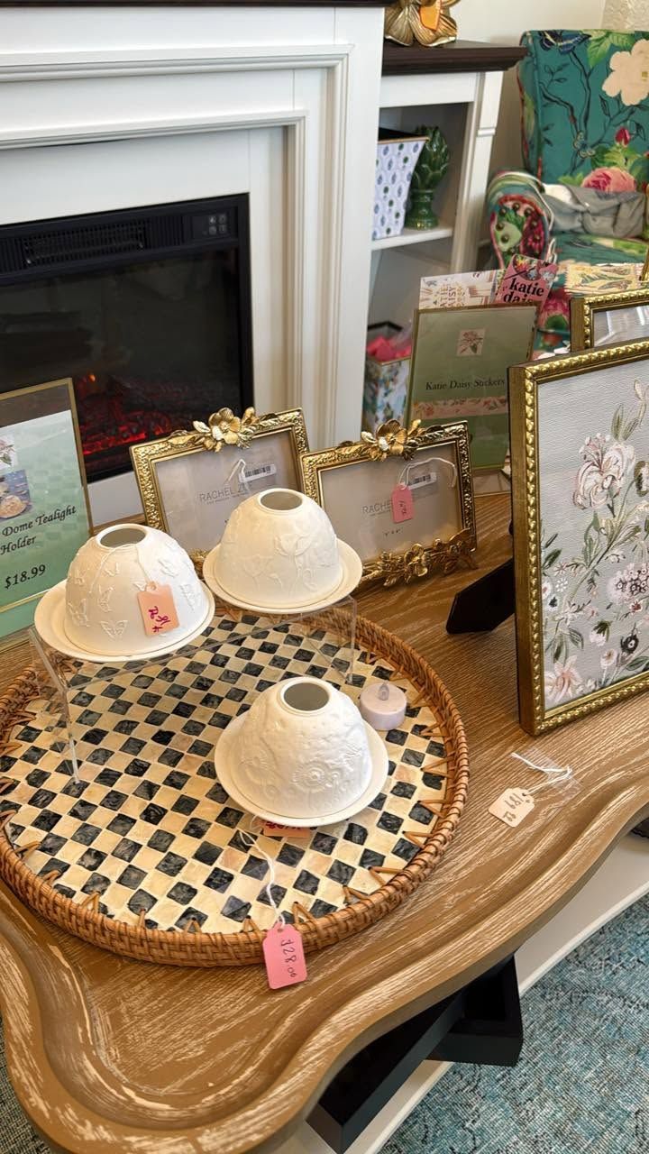 Decorative tray with four teacups and saucers on a mantel beside framed floral art and a fireplace