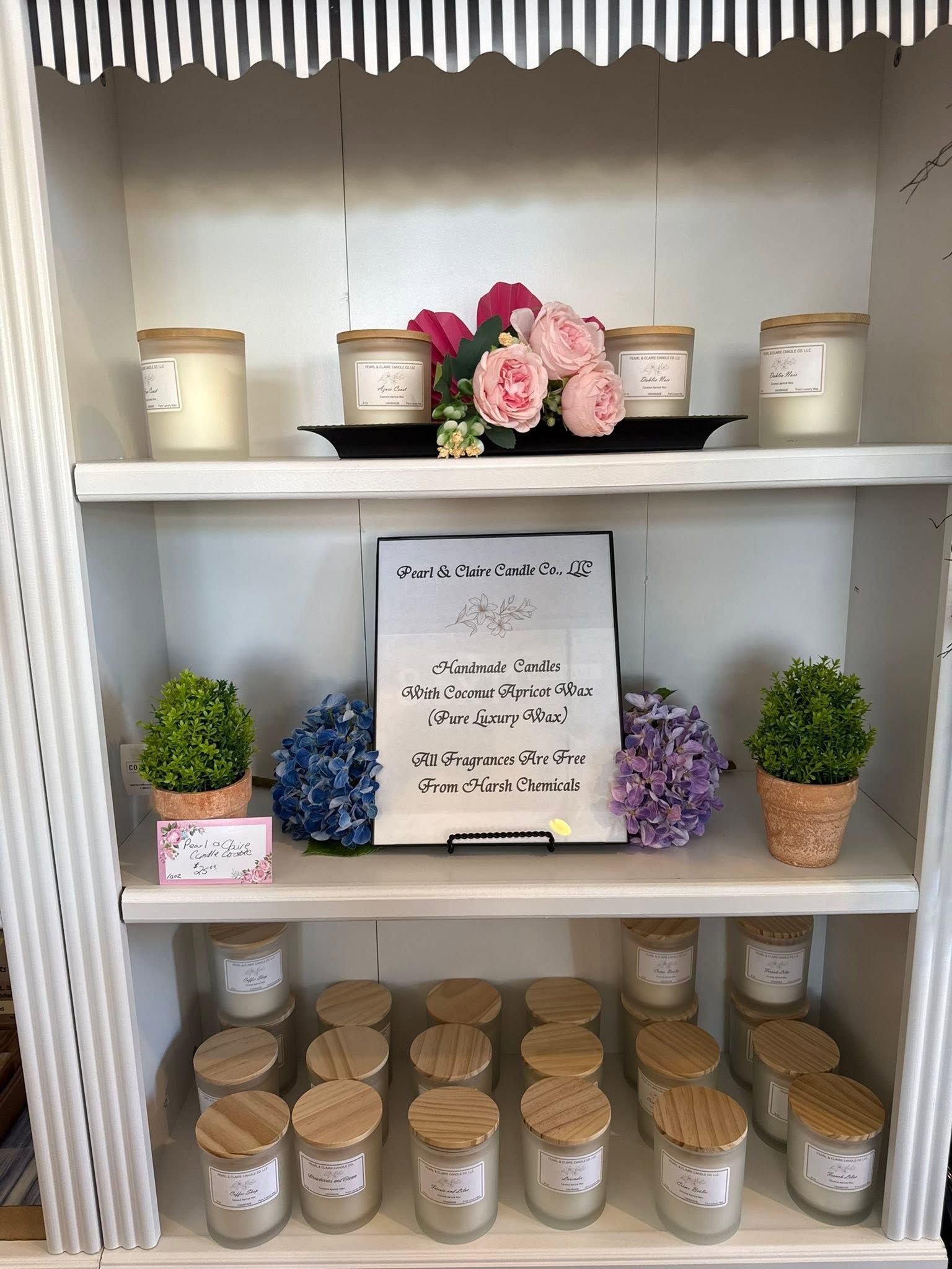 White display shelf with jars, flowers, small plants, and a handwritten sign.