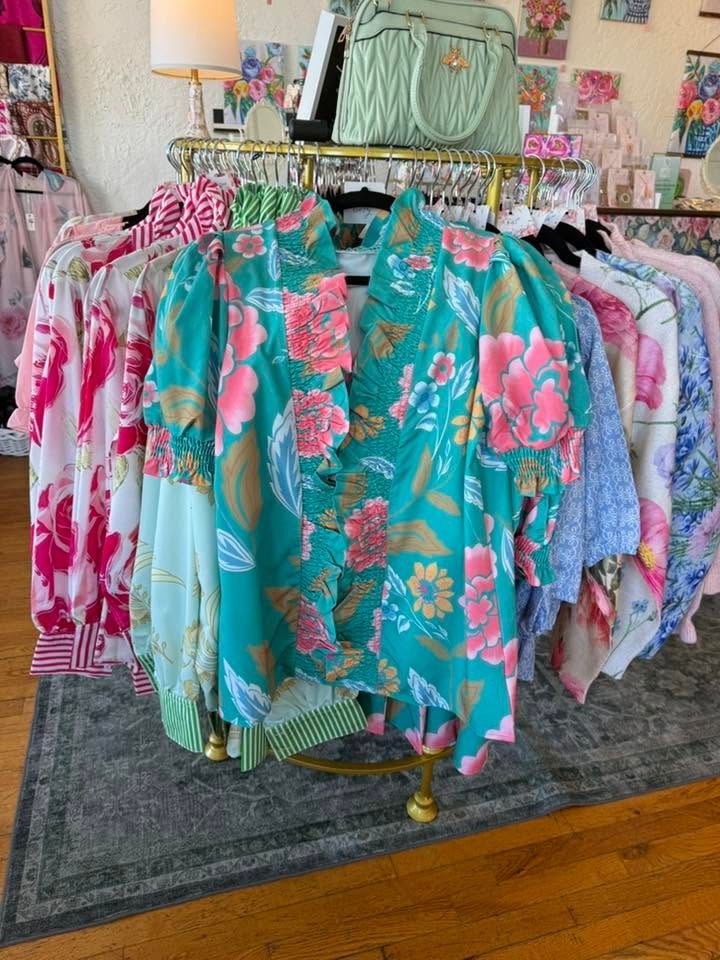Colorful floral blouses and dresses displayed on a boutique clothing rack, with a handbag above.