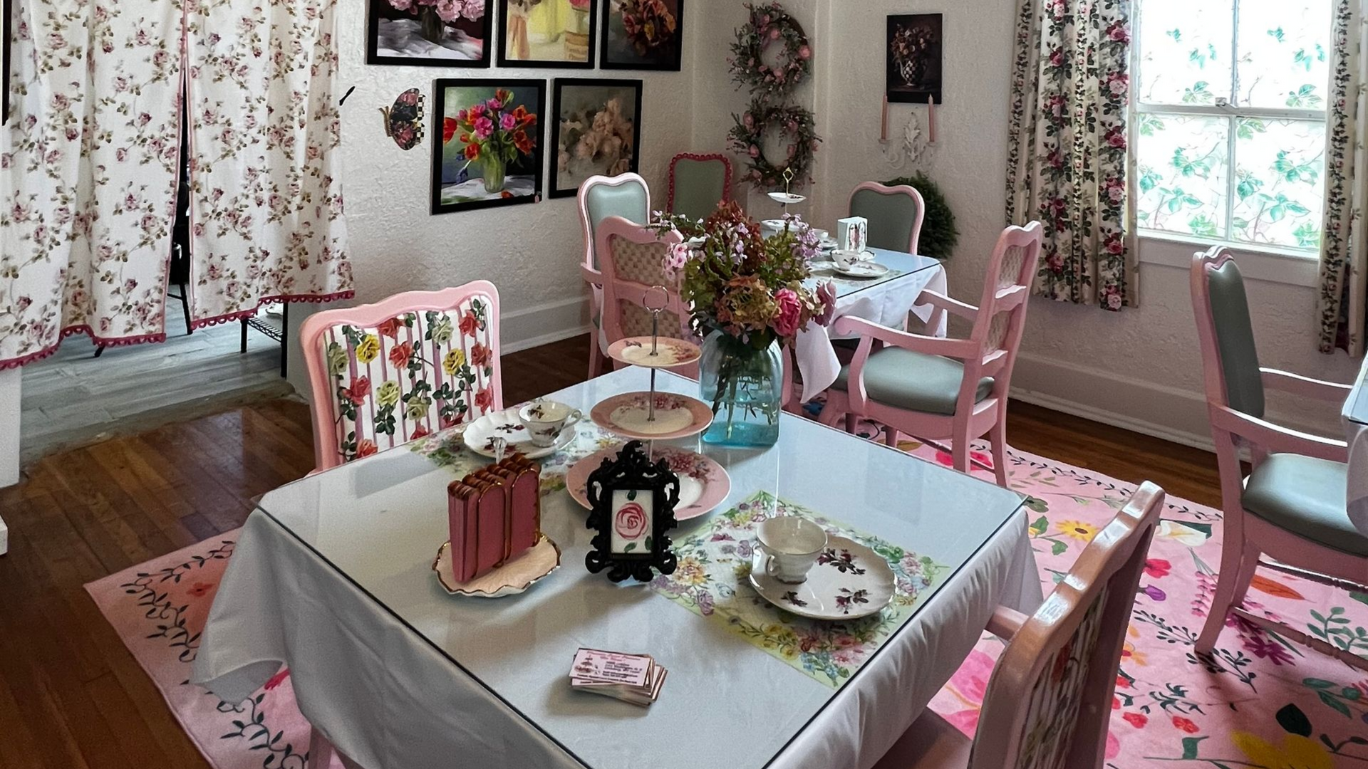 Pink-themed tea room with floral decor, chandelier, and pastel table settings by a bright window
