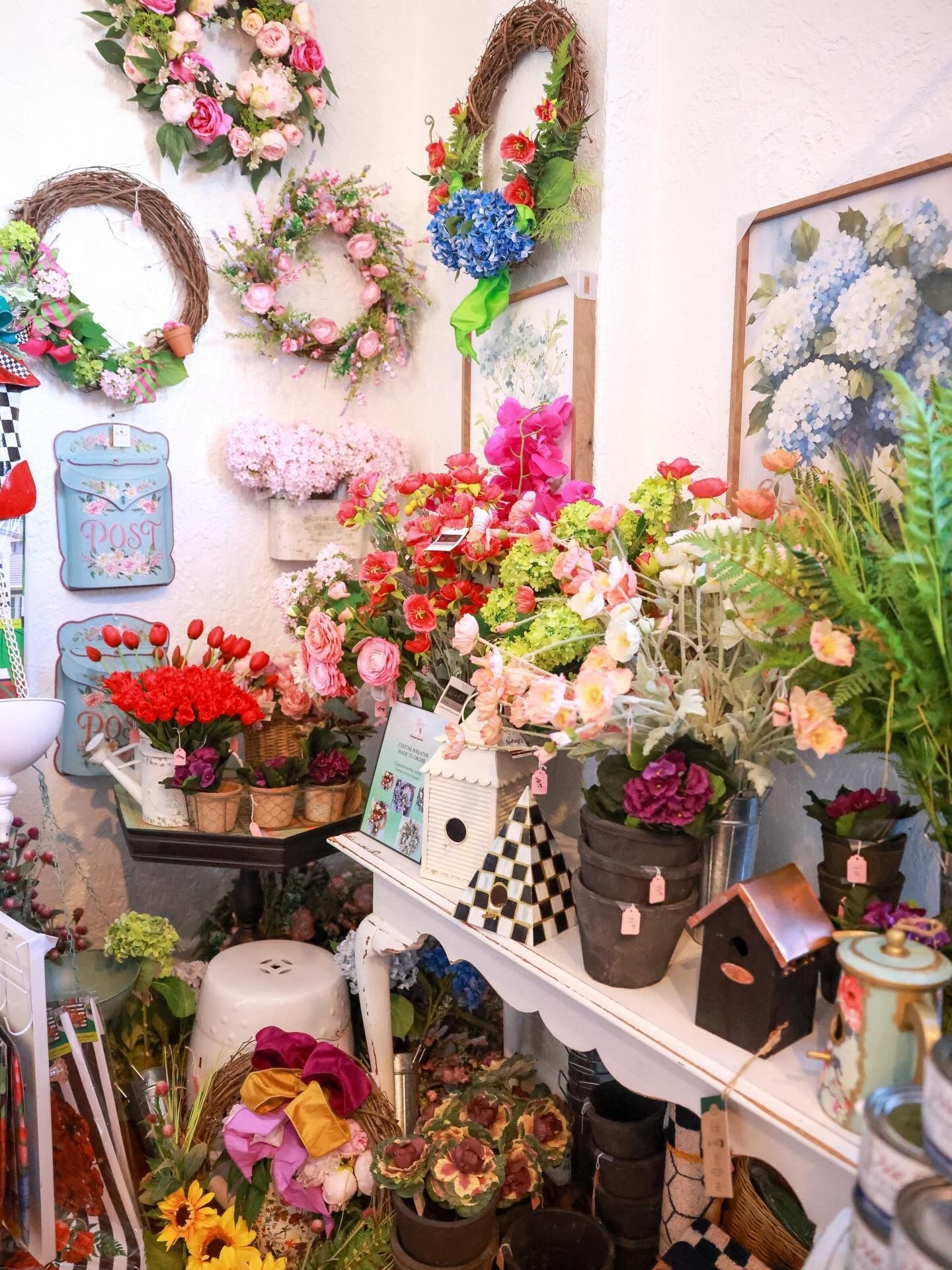 Flower shop display with colorful bouquets, wreaths, and potted plants on shelves and tables