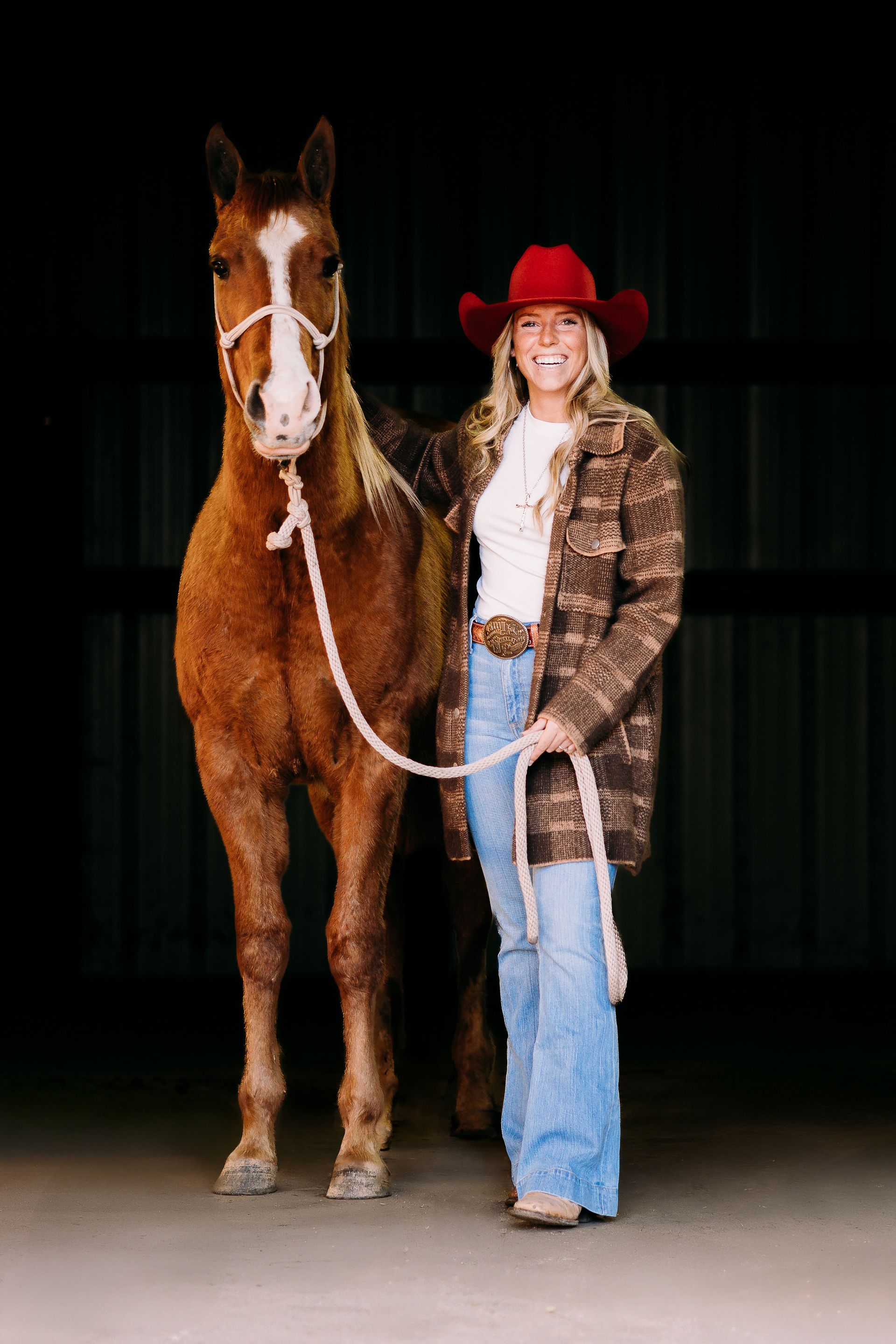 A woman in a cowboy hat is standing next to a brown horse.