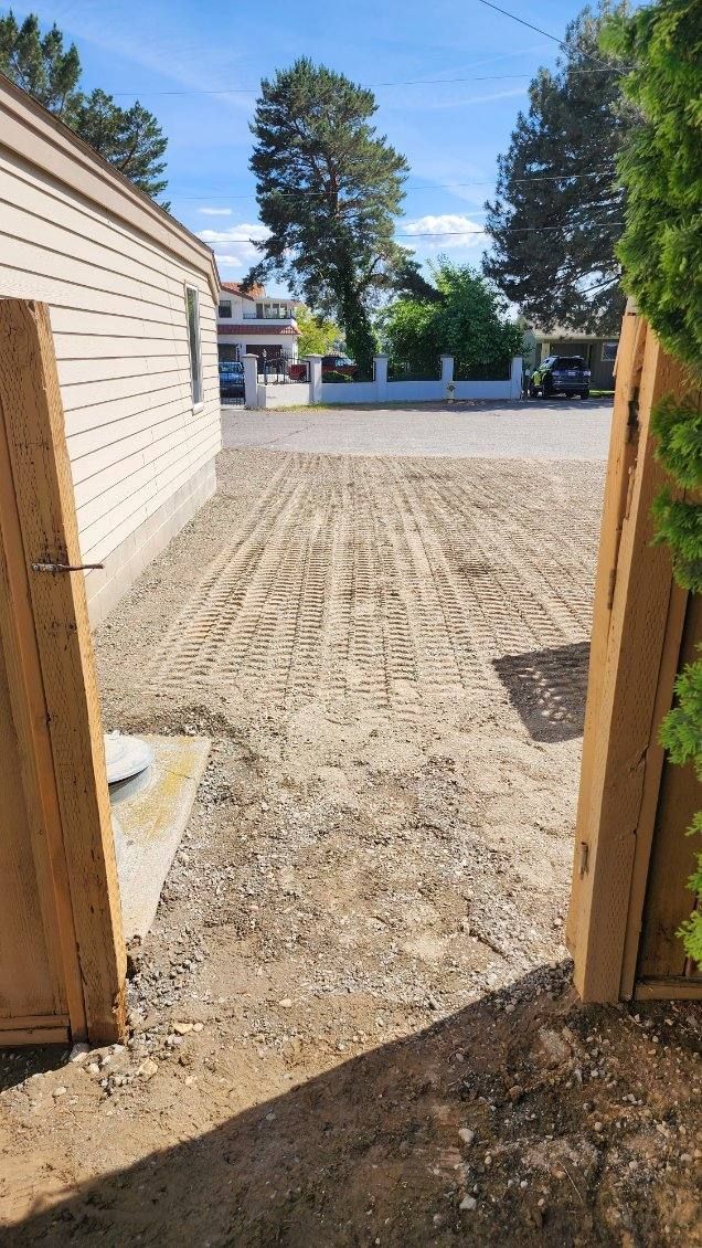 View through a doorway to a sandy yard with trees, a fence, and buildings under a clear blue sky