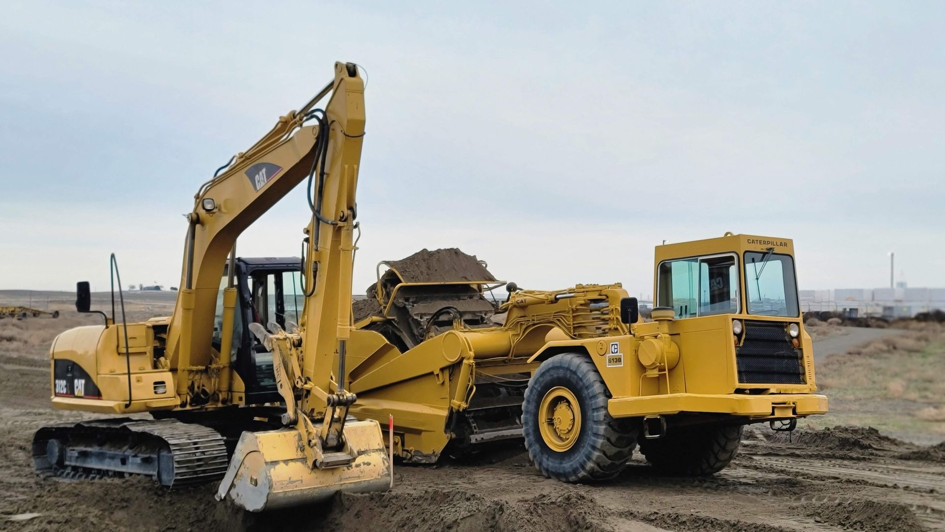 Yellow backhoe loader and dump truck on a construction site under a cloudy sky