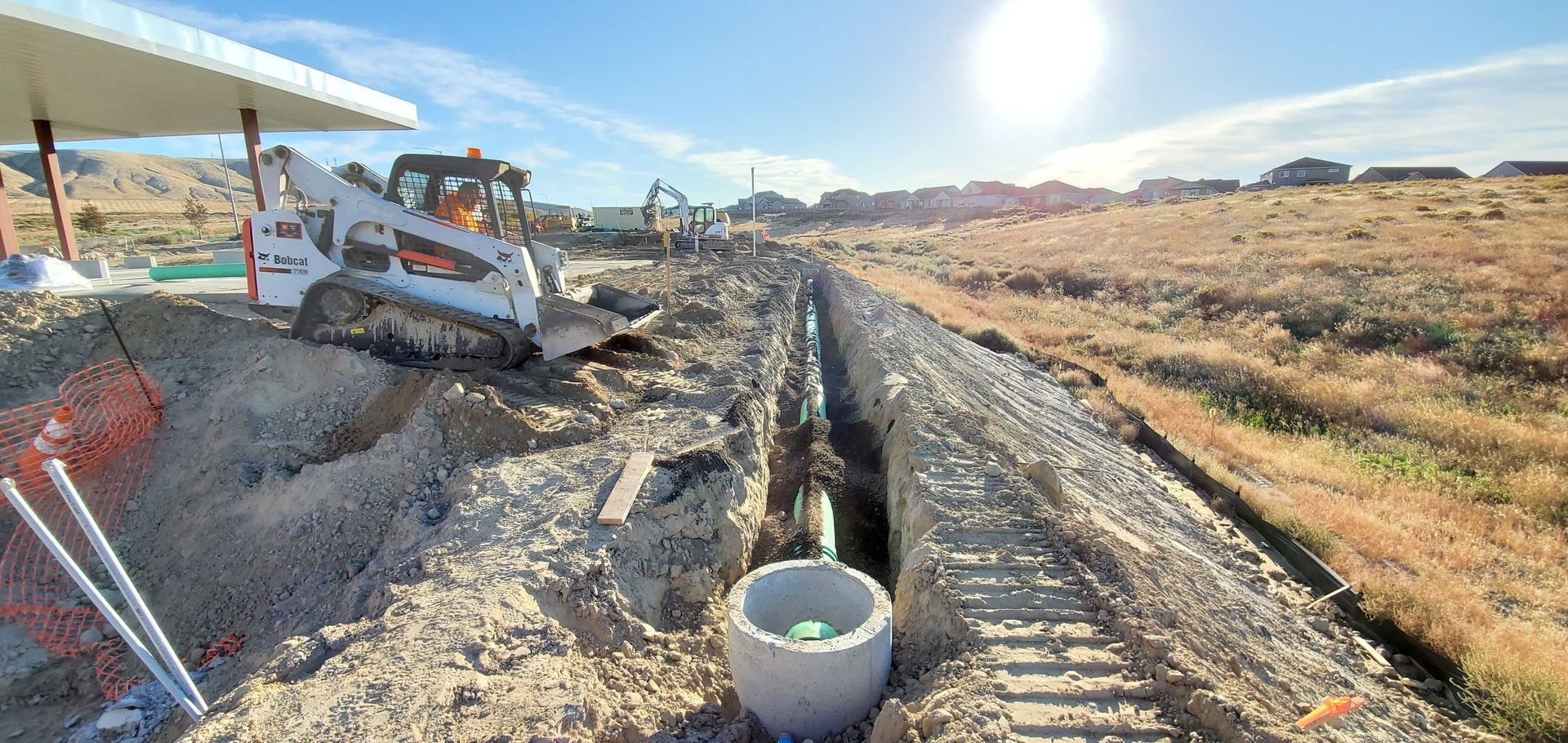 Construction site with trench, excavator, and worker in hard hat under bright sun