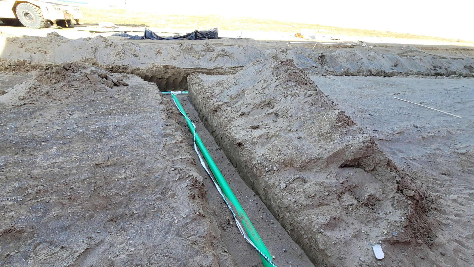 Trenched dirt site with a green pipe running through a narrow excavation