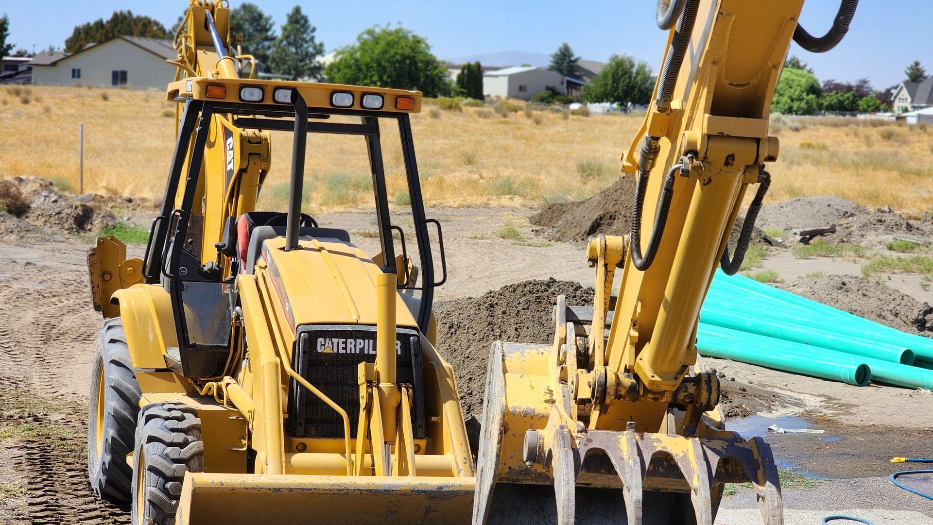 Yellow backhoe loader and excavator at a construction site with dirt and pipes