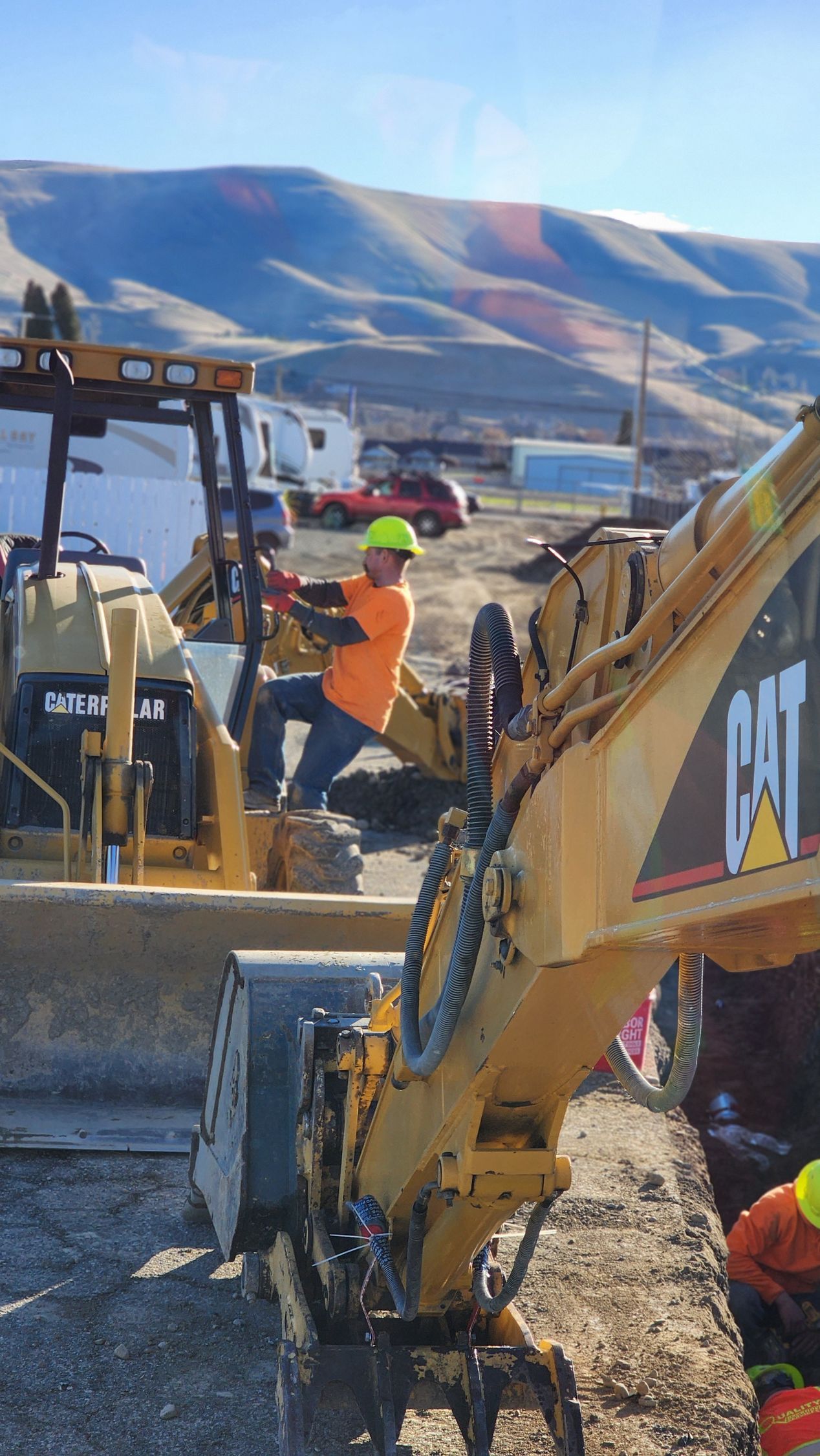 Construction workers operating heavy machinery on a dirt site with mountains in the background