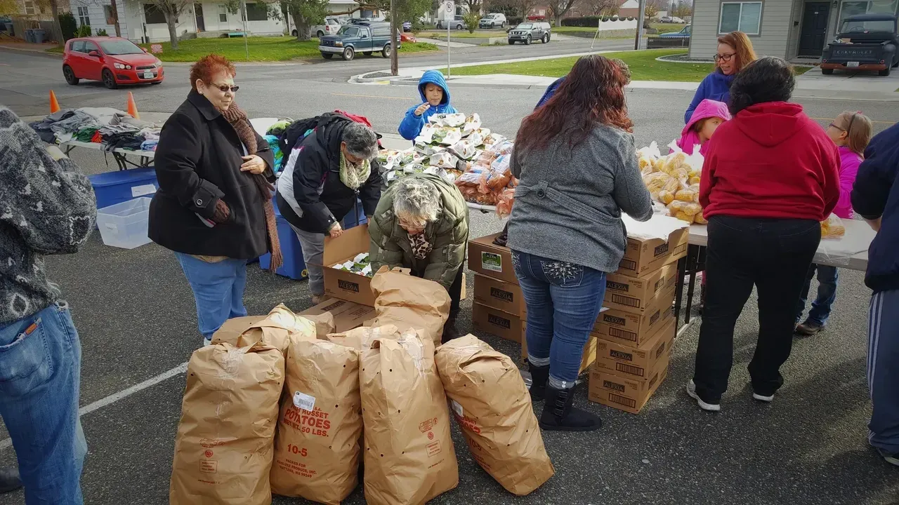 Volunteers sorting and stacking bagged donations outdoors on a wet pavement near parked cars