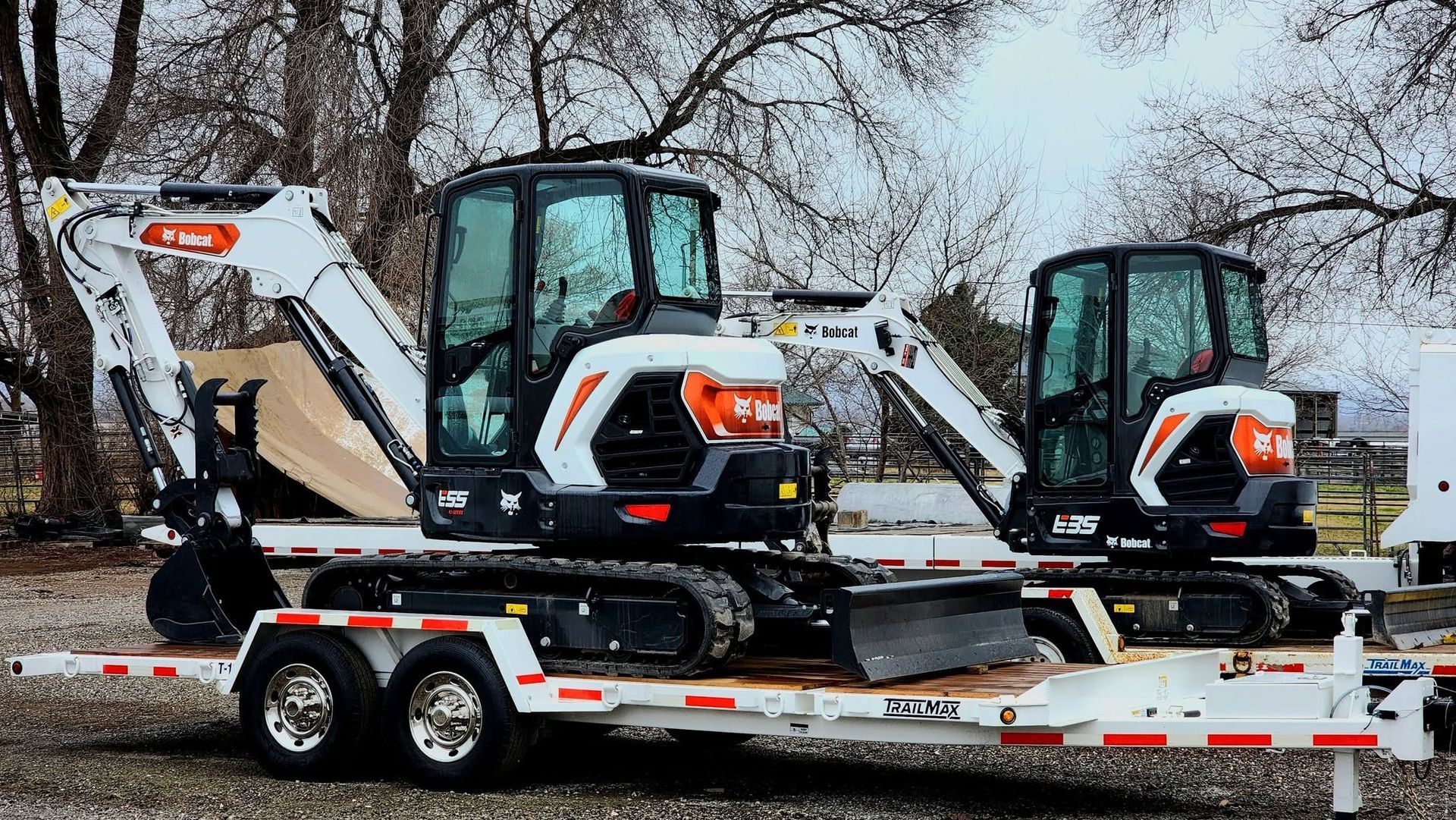 Two compact excavators on a flatbed trailer in a snowy outdoor lot