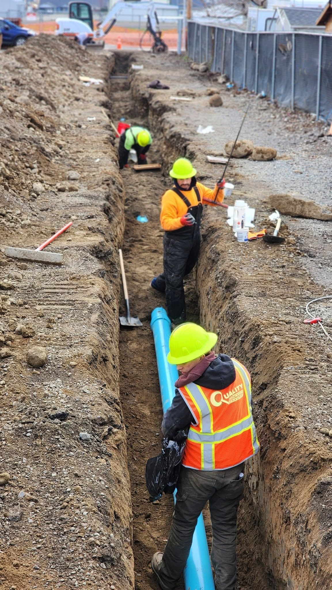 Construction workers in orange vests and yellow hard hats laying blue pipe in a trench