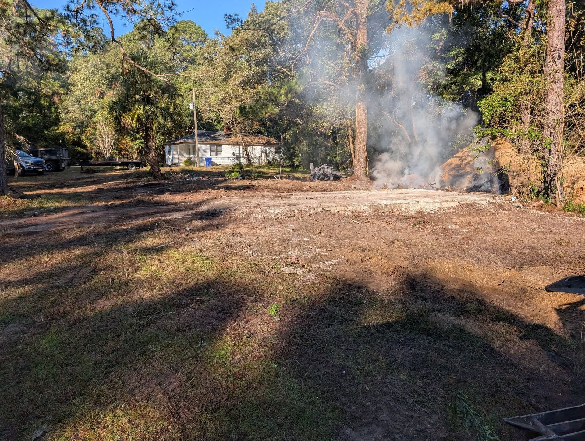 Backyard brush fire with smoke rising among trees on a sunny day