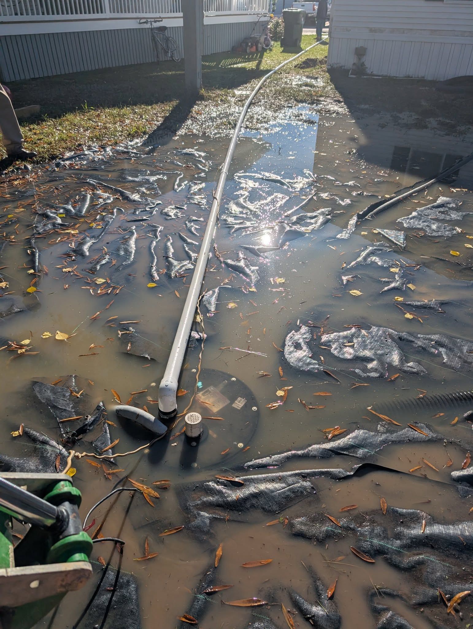 A muddy flooded yard with scattered debris and a long white pole lying across the water.